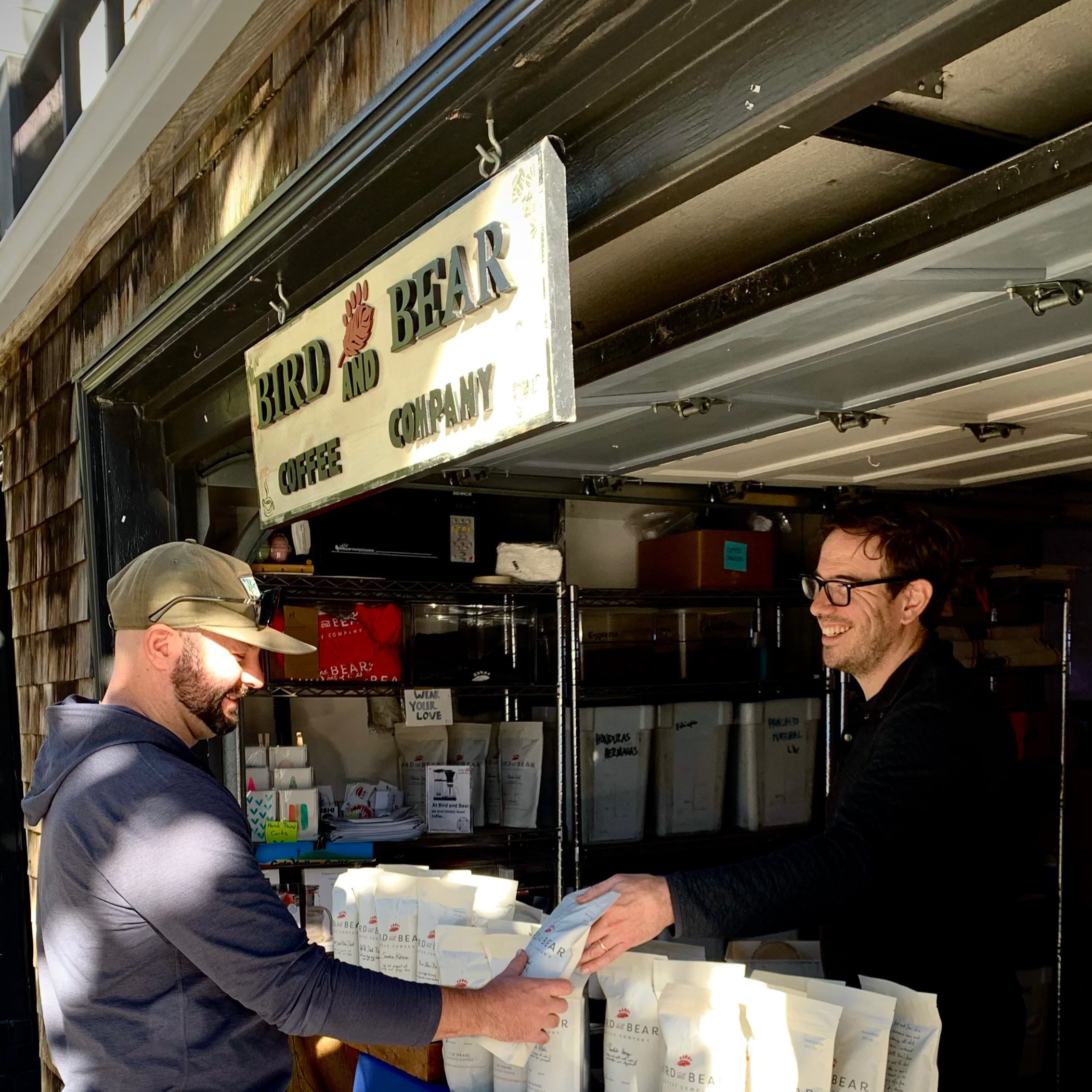 Two men with a table full of bags of coffee outside a store named 'Bird and Bear'.