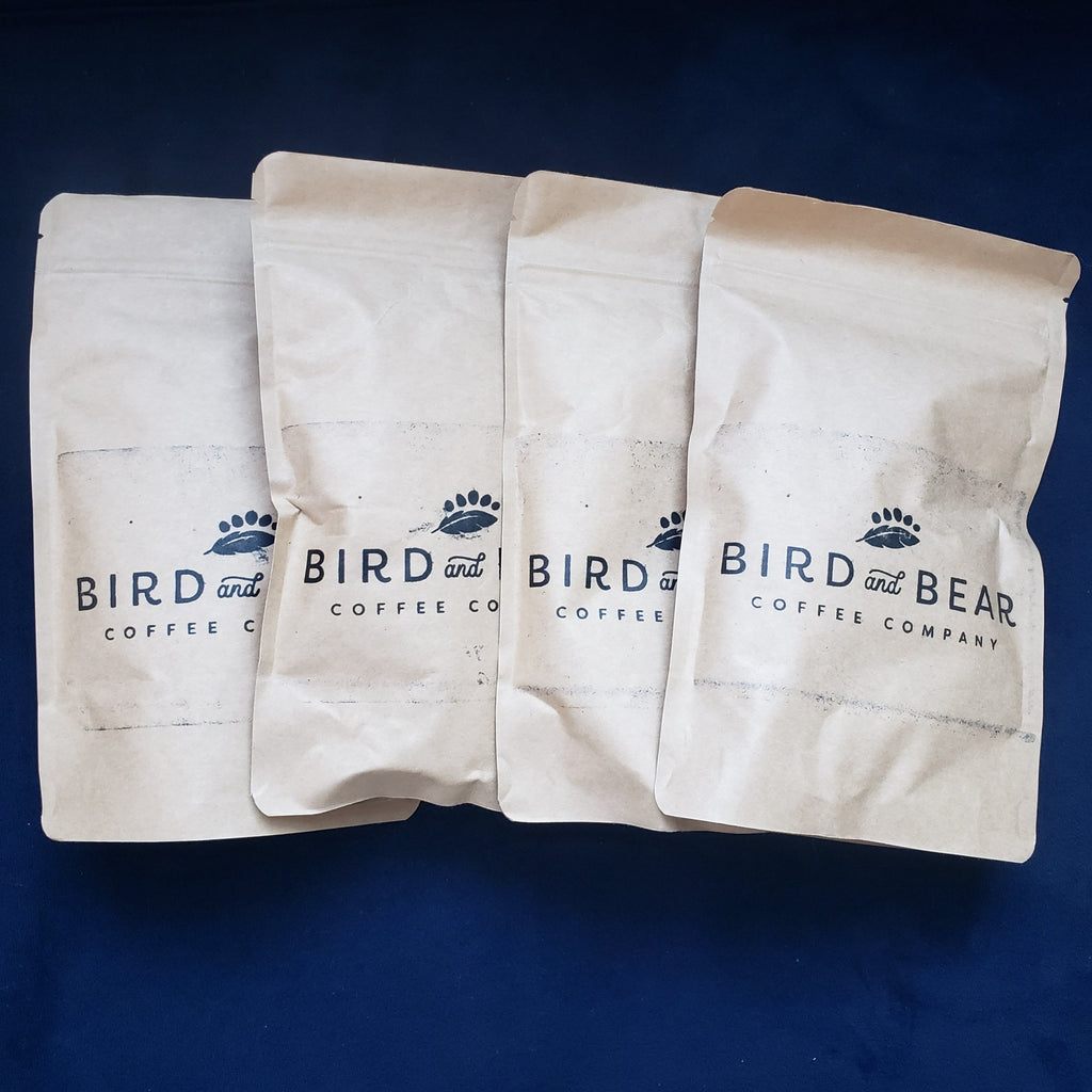 four sample size brown bags from Bird and Bear Coffee stacked on a plush navy blue background