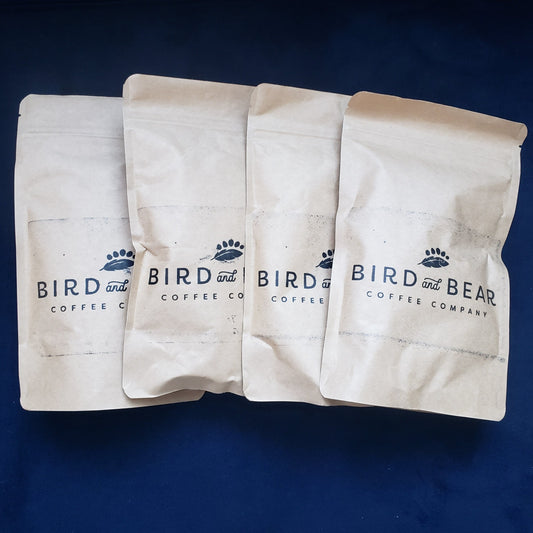 four sample size brown bags from Bird and Bear Coffee stacked on a plush navy blue background