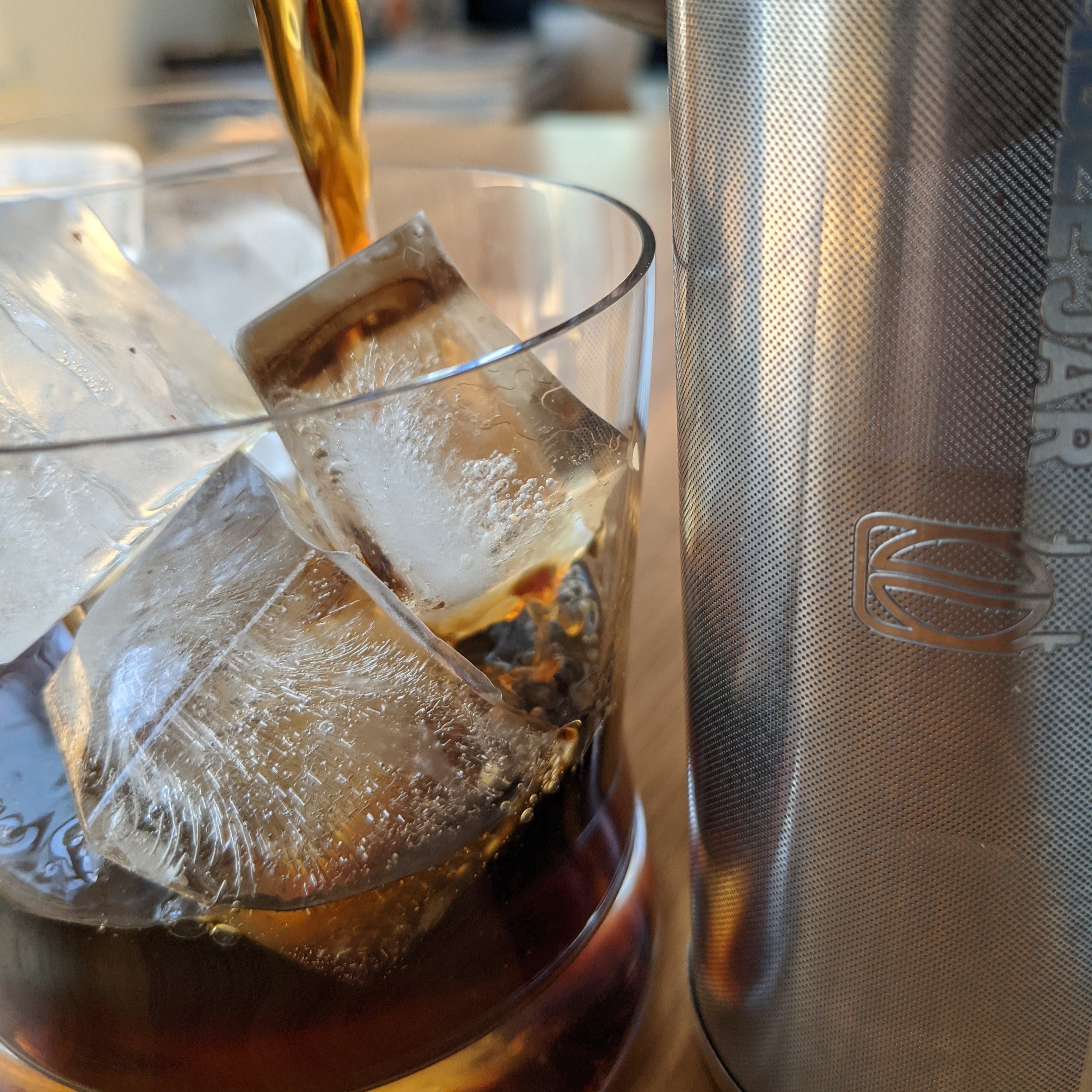Cold brew coffee being poured over ice, into a rocks glass alongside the rumble jar cold brew coffee filter.